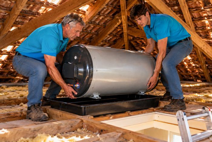 Two technicians setting a new geyser onto its drip tray in the roof space