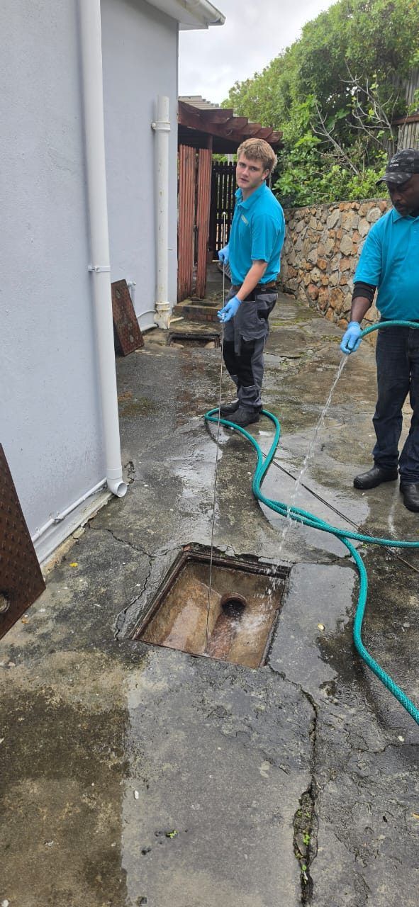 Lightning Fast plumber clearing a blocked main drain with a drain rod while a colleague flushes it with a hose