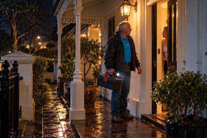 Technician arriving at a front door at night in the rain, torch and toolbox in hand